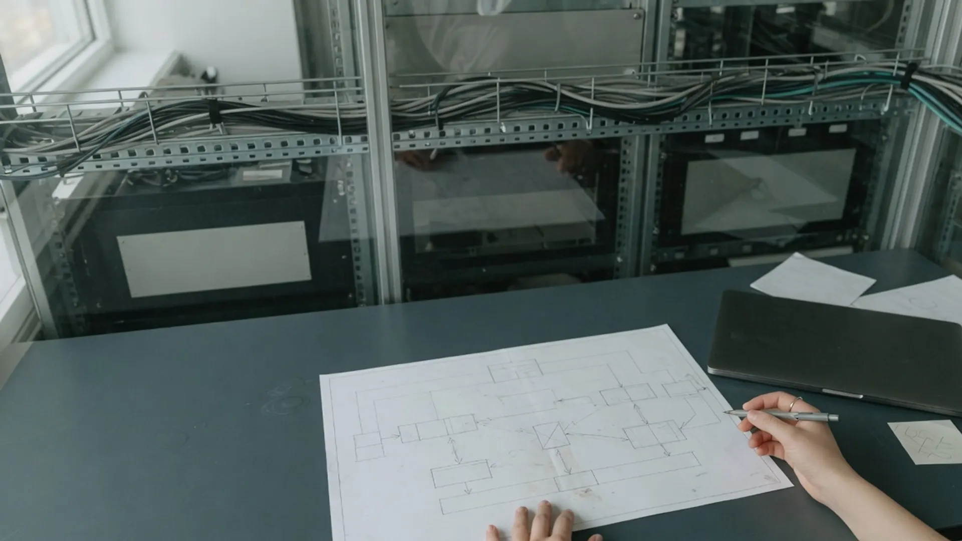 Server room adjacent workspace with unmarked cutover notes and network diagrams